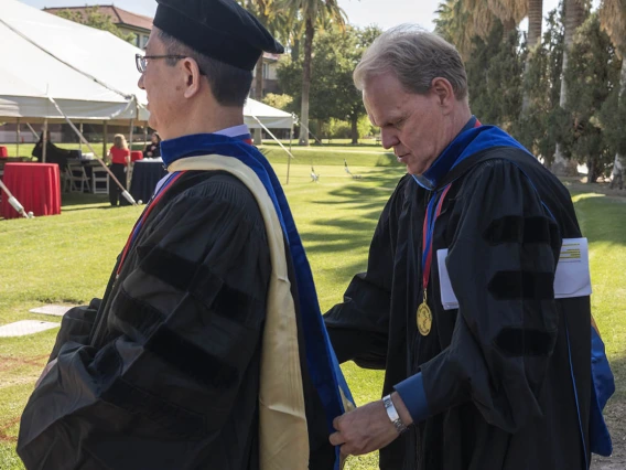 R. Ken Coit College of Pharmacy director of graduate studies, Georg Wondrak, PhD, (right) helps adjust the hood on Xinxin Ding, PhD, department head, Pharmacology and Toxicology, before the start of the 2022 spring convocation at Centennial Hall.