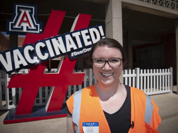 Leslie Farland, ScD, assistant professor at the Mel and Enid Zuckerman College of Public Health, poses by a sign at the Pima County POD at the University of Arizona to encourage others to receive COVID-19 vaccinations.