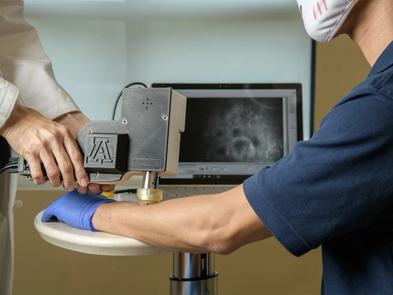 Clara Curiel Lewandrowski, MD, uses a portable skin cancer diagnostic microscope on Dongkyun Kang, PhD, to test the output image on a laptop screen. The two are developing the device to enable faster skin cancer diagnosis in doctor’s offices.