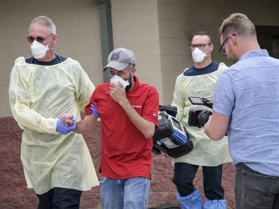 Erich Healy, right, films as Tucson Fire Department’s Chris LaFave, left, helps guide Jonathan Sexton, PhD, who is playing a possible COVID-19 patient in a training video, into an ambulance.