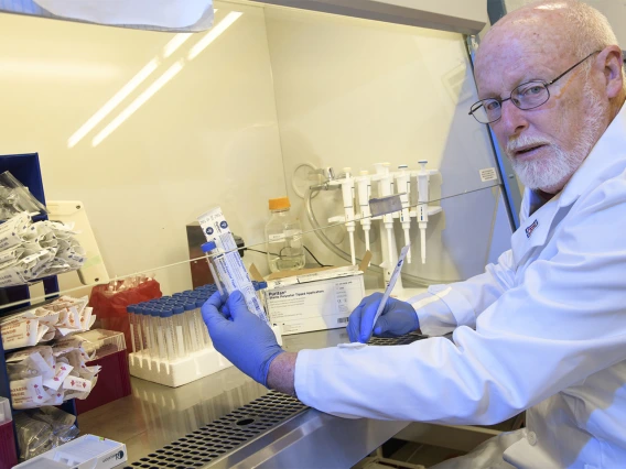 David T. Harris, PhD, holds up items from a sample collection kit under a serial hood. 