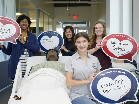 4 women stand around a patient manikin holding heart posters