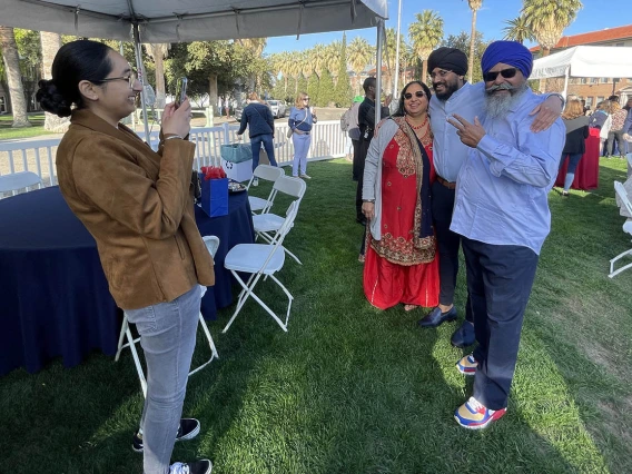 A young man with his parents on either side of him stand for a photo. The two men have headwraps on and beards. 