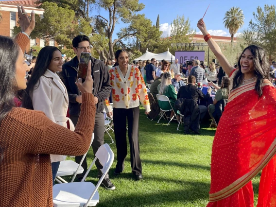 Woman in red sari poses with arms out while family members take photos.