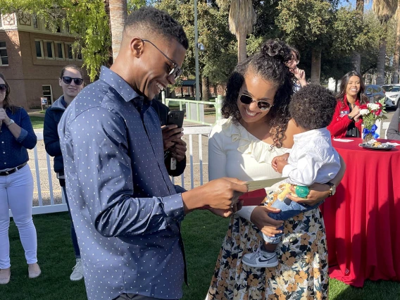 Young dark-skinned doctor shows his match day envelop to his wife and child.