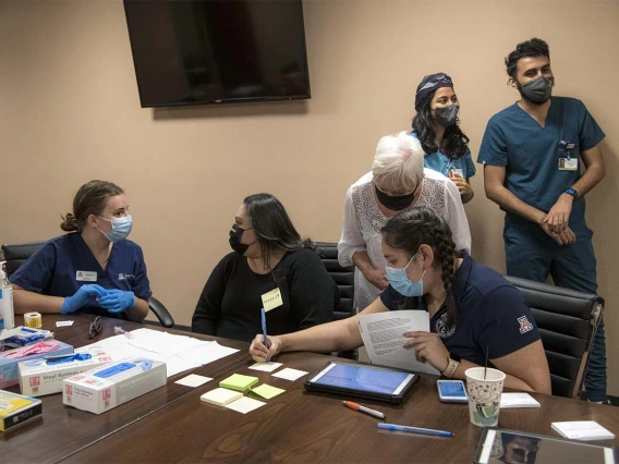 Public Health student and scribe Diana Grijalva (on right in front) writes as College of Nursing preceptor Nancy McGuckin, RN, MSN, MPH (standing with white hair) advises her. On the left, Nursing student Valerie Pedersen prepares to vaccinate a patient (center). Behind (on right) are College of Medicine senior students Maya Sarihan and Abdullah Aleem, who also participated as vaccinators.