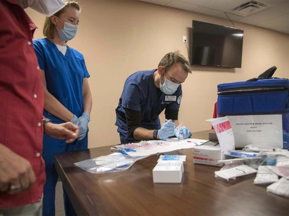 College of Nursing student Graham Robinson gets instruction on how to measure an appropriate dosage of the COVID-19 vaccine to be administered to patients at a MOVE UP clinic at the Consulate of Mexico in Douglas in partnership with the UArizona Health Sciences  and Cochise County Health Department. Fellow Nursing student Jane Leahy is to left of him.