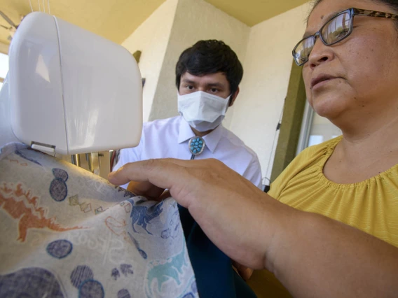 University of Arizona College of Medicine – Tucson student Aaron Bia watches as Navajo seamstress Theresa Hatathlie-Delmar sews a surgical cap with material donated in the college’s PPE drive.