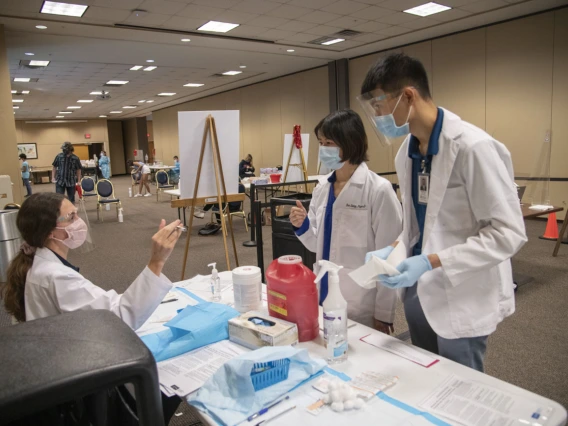 College of Pharmacy students Catherine Hensley (left) and Sang Nguyen (right) consult preceptor Eva Liang, PharmD (center), about techniques for administering a shot.