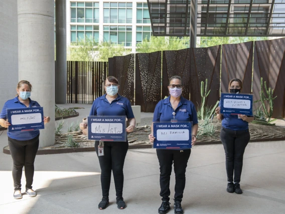 Alicia Espinoza, Bertha Chavez, Sandra Romo and Altagracia Coronado, who provide building services for the Phoenix Biomedical Campus, hold their signs in a courtyard.