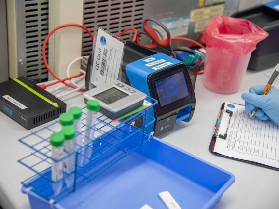 Lab tech Jennifer Alvarado places a cassette with a person's nasal swab sample into the machine that will process it and determine whether the person is positive or negative for COVID-19. This blue machine takes 11 seconds to produce a result, and a person is notified of their results via email within two hours of taking the test.