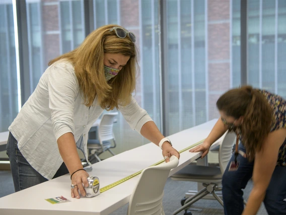 Angie Souza (left) and Jill Garcia (right) of Health Sciences Planning and Facilities measure the distance between desks in the Health Sciences Innovation Building to calculate new seating requirements, ensuring people stay six feet apart.