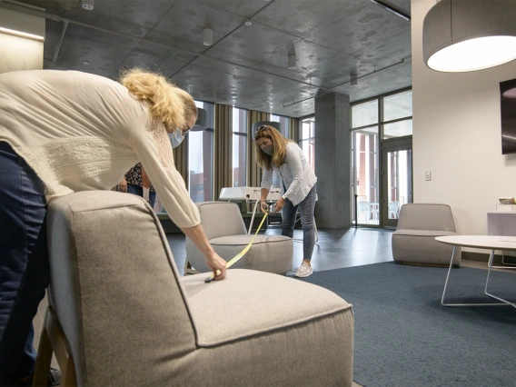 Mary Matthews (left) and Angie Souza (right) of Health Sciences Planning and Facilities measure the distance between chairs in a student lounge in the Health Science Innovation Building to ensure that the placement of furniture facilitates adequate physical distancing.