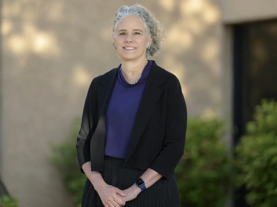 Portrait of a smiling light-skinned woman with curly gray hair standing outside. 