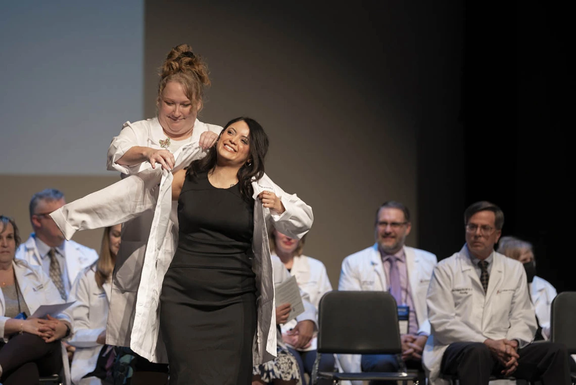 Professor Jennifer Hunter in the University of Arizona College of Nursing, helps Xitlali Arias-Ortiz into her coat at the college’s white coat ceremony.