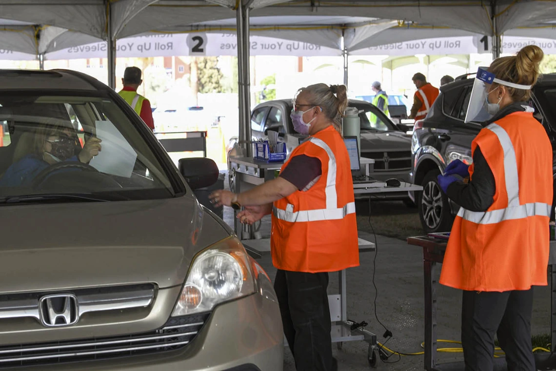 Volunteers Becky Dillie, center, Kerry Johnson, right, collect paperwork from drivers awaiting their vaccine.