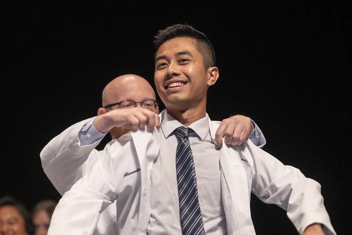 A young Asian man with a big smile is presented with his Pharmacy white coat. 