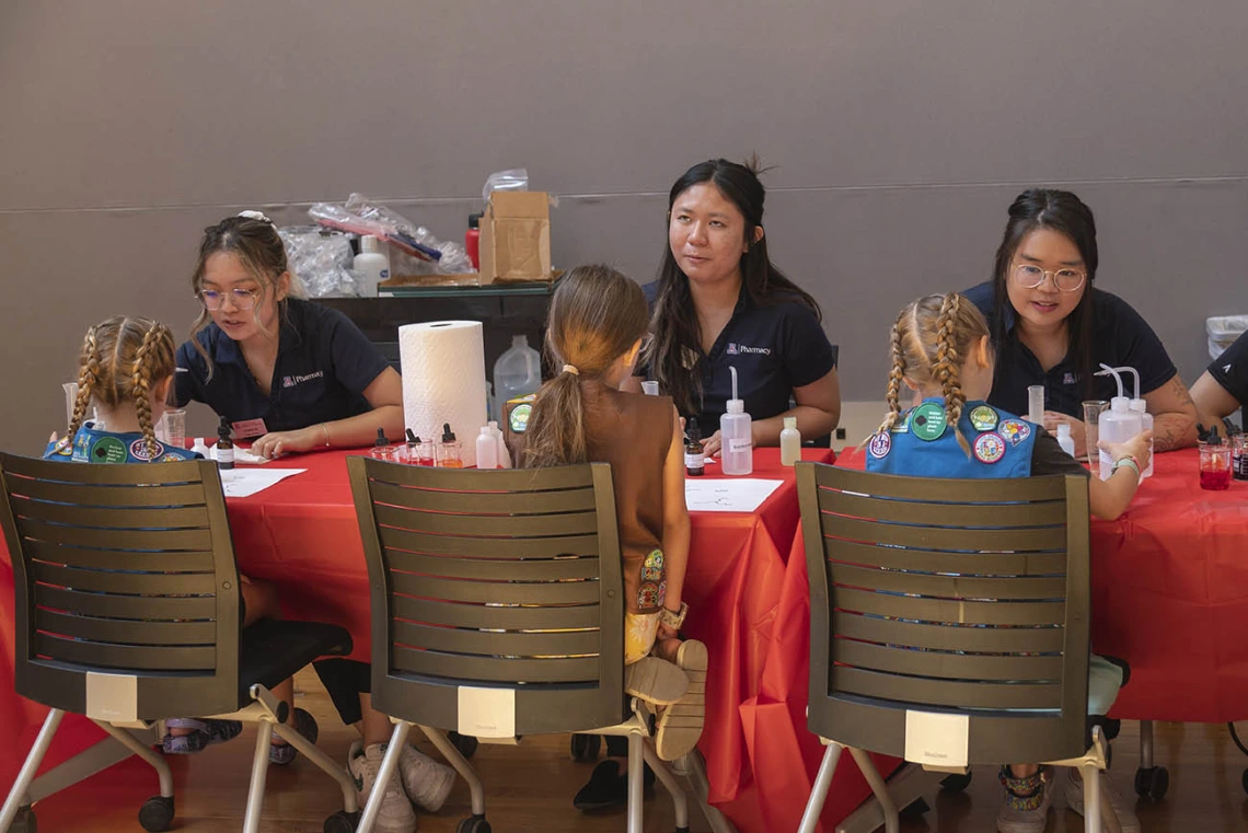 Three female pharmacy students set at a table each facing a girl scout doing an activity with them.