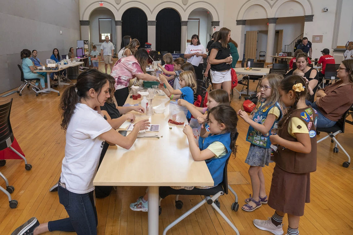 A large room filled with activity tables, volunteers and girl scouts. 