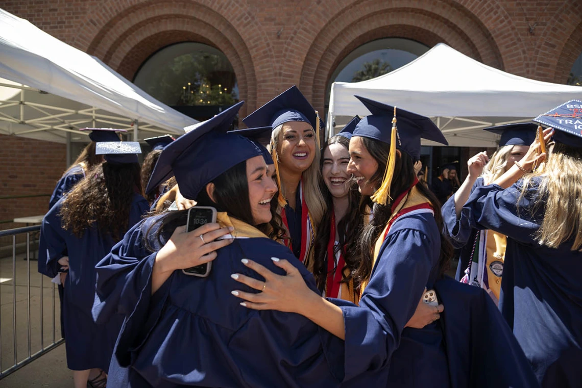 A group of young women wearing cap and gown celebrate together in a group hug after their convocation. 