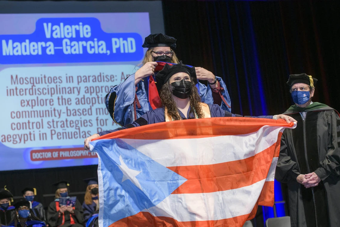 Valerie Madera-Garcia, PhD, holds the Puerto Rican flag as she is hooded during the 2022 Mel and Enid Zuckerman College of Public Health spring convocation for earning a doctorate in epidemiology.