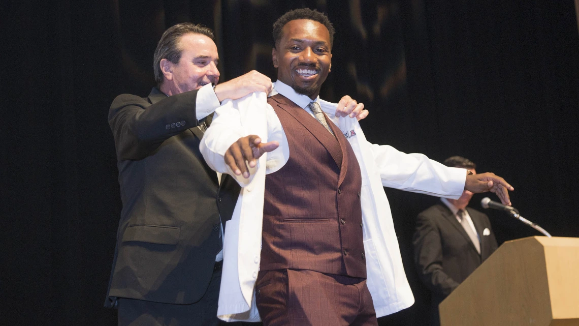 Paul R. Standley, PhD, associate dean of curricular affairs and program evaluation at the UArizona College of Medicine – Phoenix, presents Javon Maceo Freeman with his white coat.