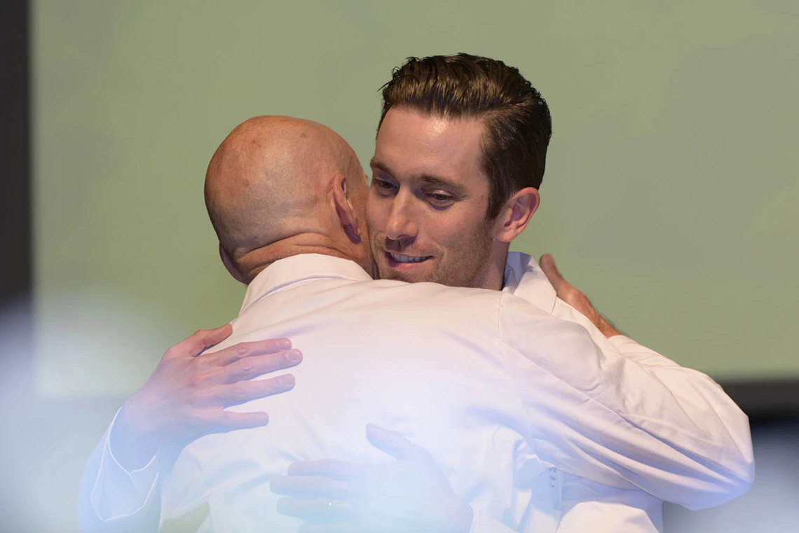 Two male medical school professors wearing white coats hug. 