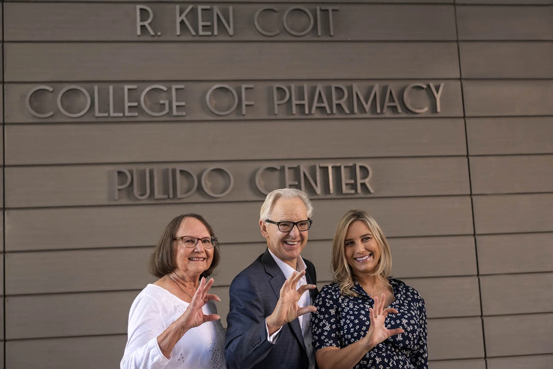 Donna Coit, R. Ken Coit and daughter Lauryn Coit Ackley give the Wildcat sign in front of the newly named R. Ken Coit College of Pharmacy. 