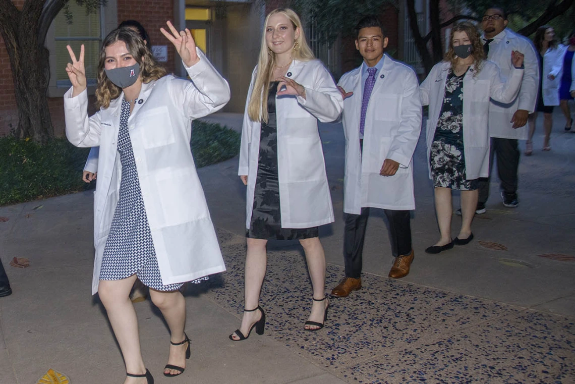 Issa Jimenez Espinoza gives two V signs as she and her classmates Megan Taylor, Brenn Belone, Lacey Hart and Curtis Mcguire leave Centennial Hall after participating in the Class of 2025 white coat ceremony.