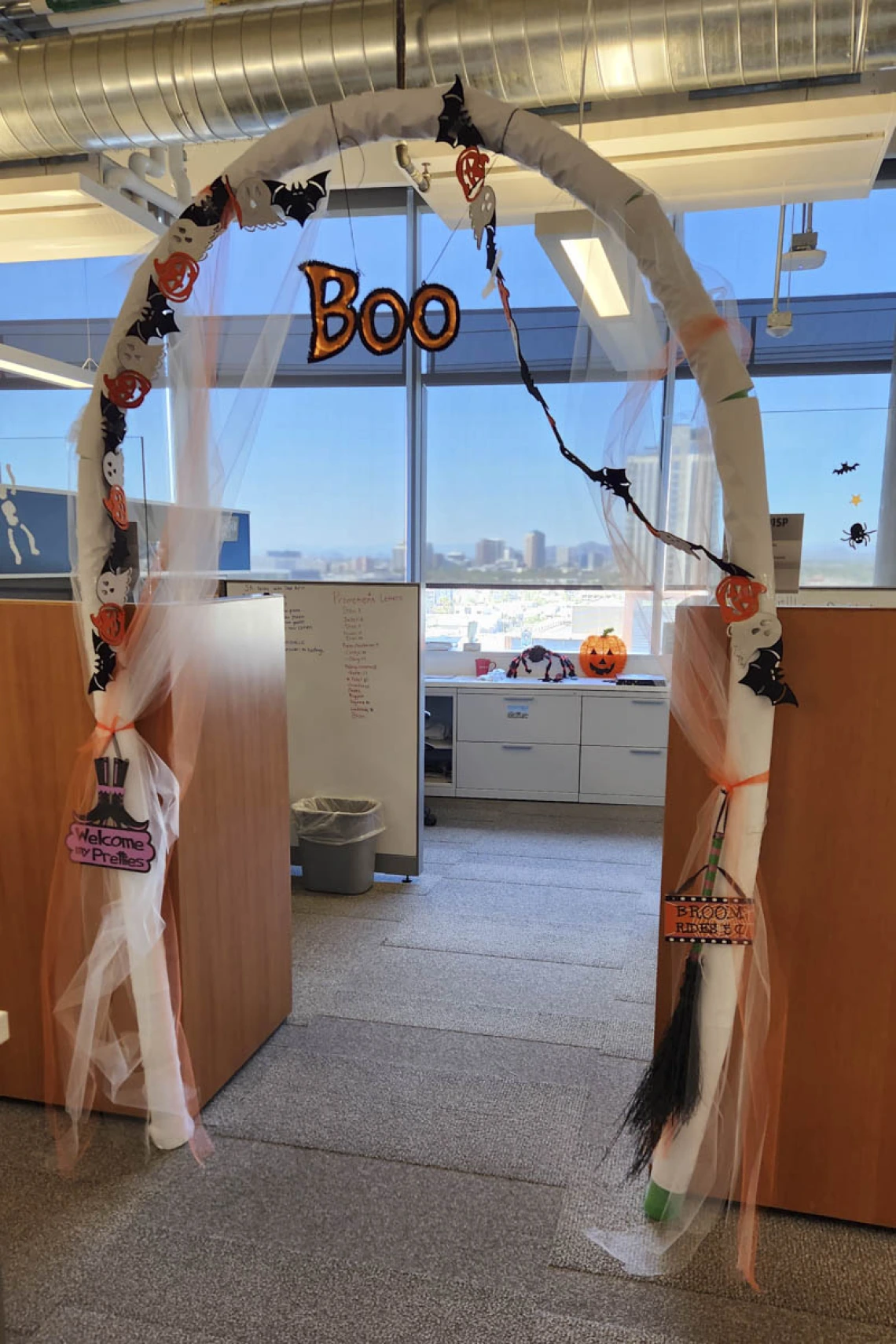 Halloween decorations create an archway between cubicles in an office. the word "Boo" hangs from the top.