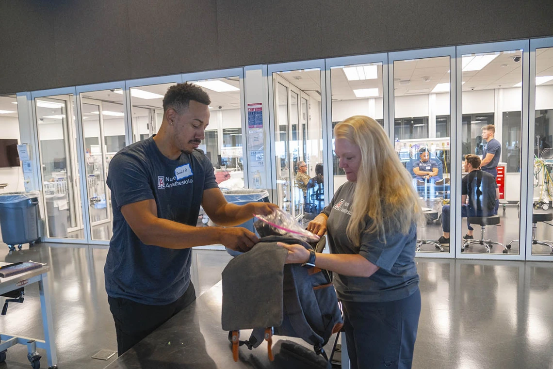 A young man stuffs donations into a backpack held by his instructor in a clinical training room.