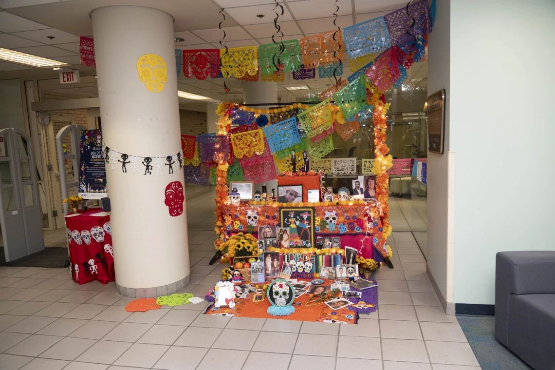 Brightly colored Dia de los Muertos altar with tissue paper flages, flowers and photos of people and animals. 