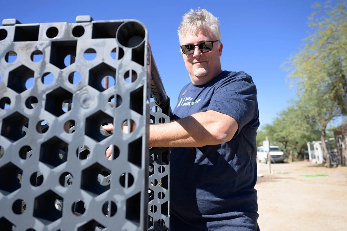 A man with short gray hair wearing sunglasses carries a shelf outside. 