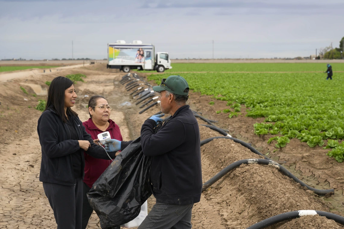 Sheila Soto and health educator Andrea Contreras, speak to a man in the middle of a farm field in San Luis, Arizona.