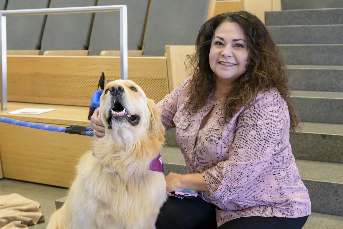 A woman sits on some stairs while petting a golden retriever, who almost looks to be smiling. 