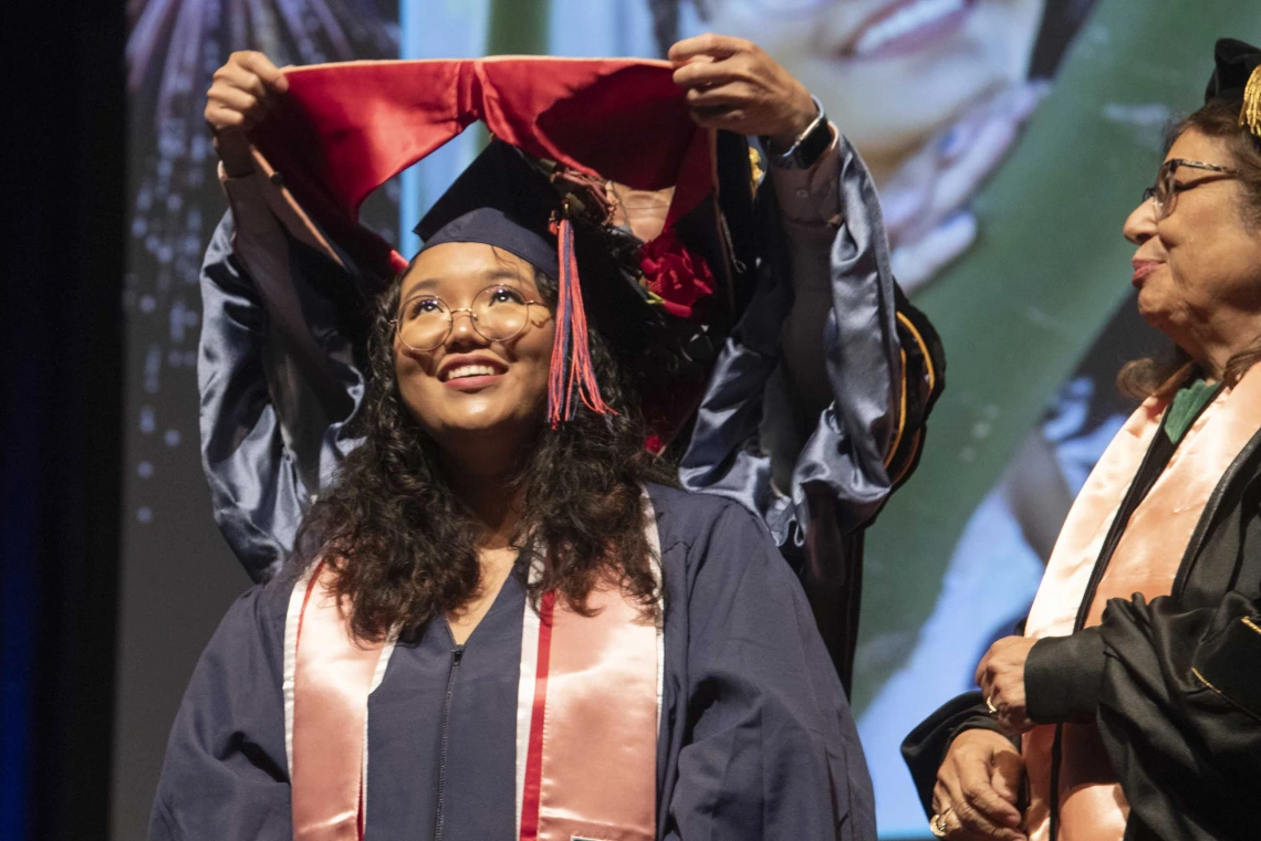 A University of Arizona Mel and Enid Zuckerman College of Public Health student smiles as she has a hood placed over her shoulders by a faculty member. 