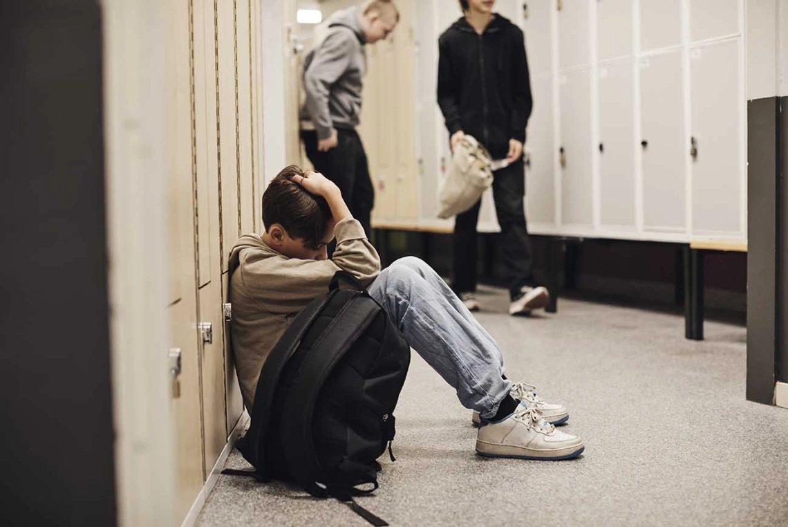 A boy sitting on the ground with a backpack in a school setting