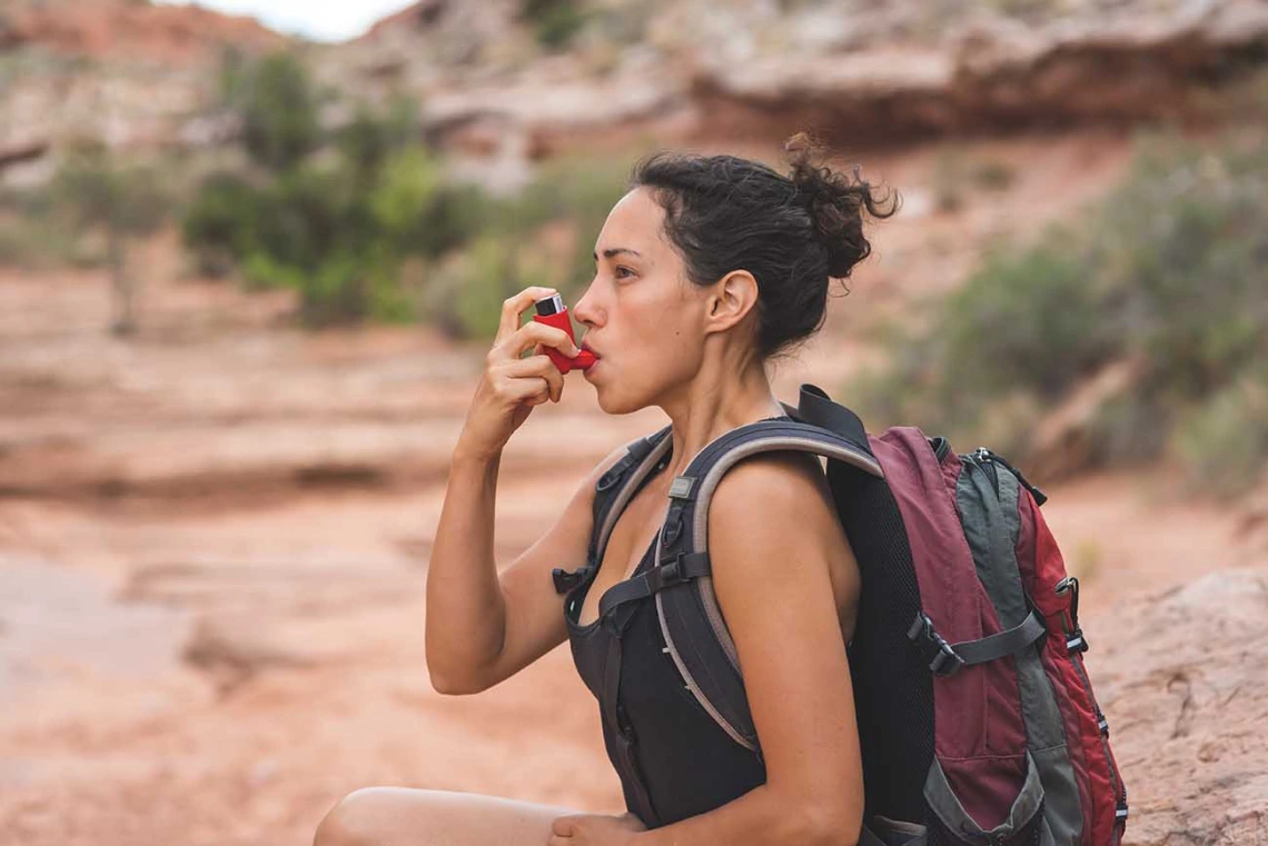 Woman with chronic asthma using inhaler while hiking in the desert