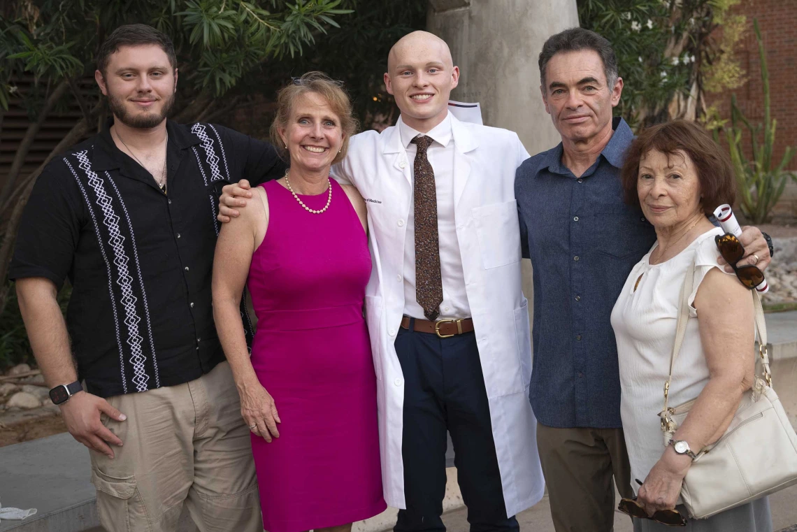 An incoming University of Arizona College of Medicine – Tucson student wearing a medical white coat stands with several family members outdoors. 