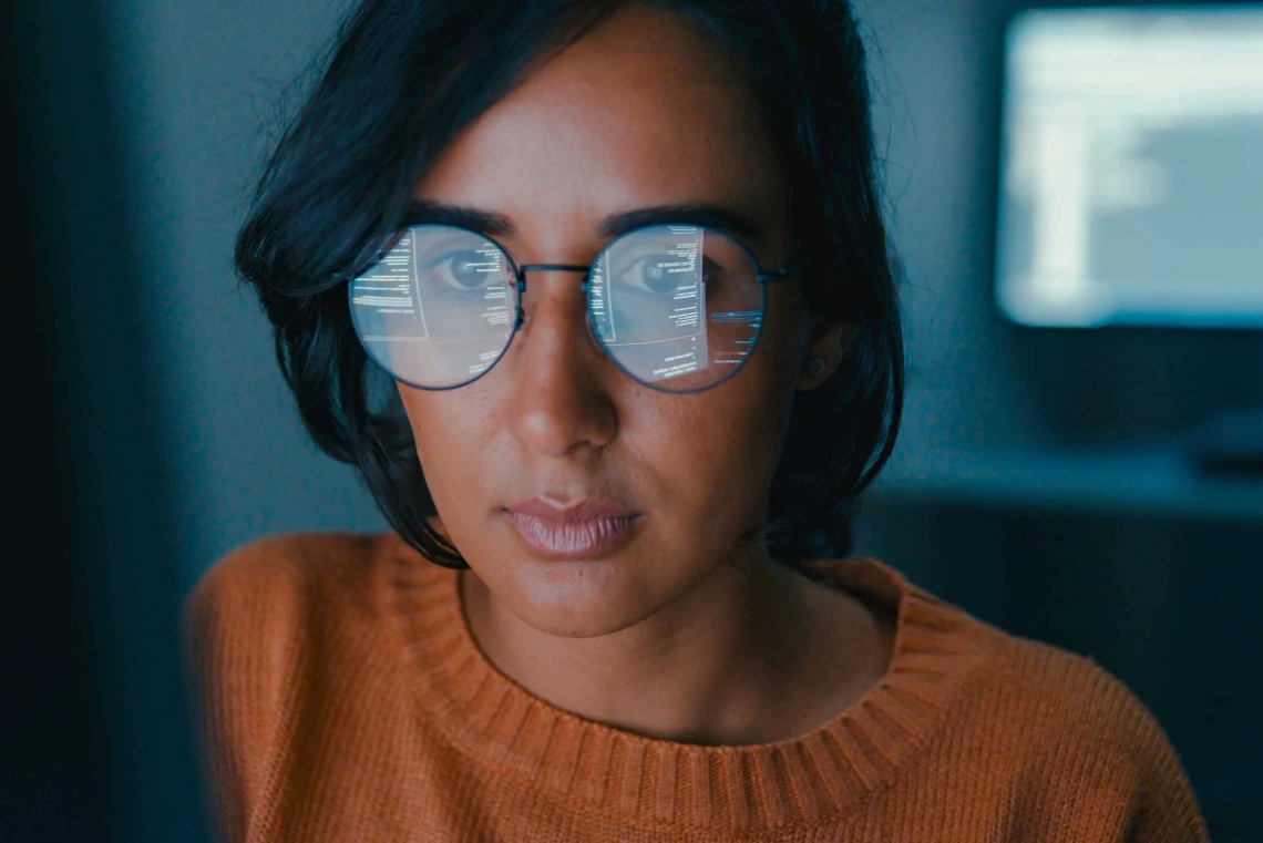 A photo illustration of a woman looking at a computer screen with words and numbers reflected in her glasses. 