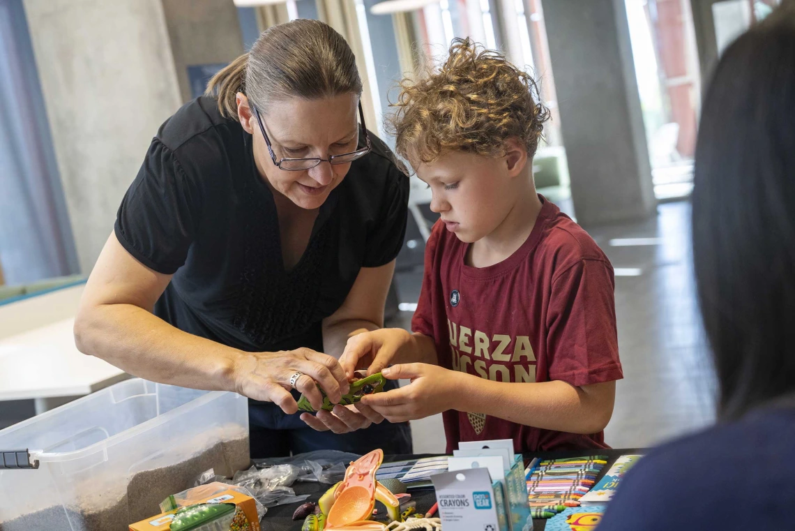 A mother and son stand at a table working on a plastic, 3D puzzle of a frog. 