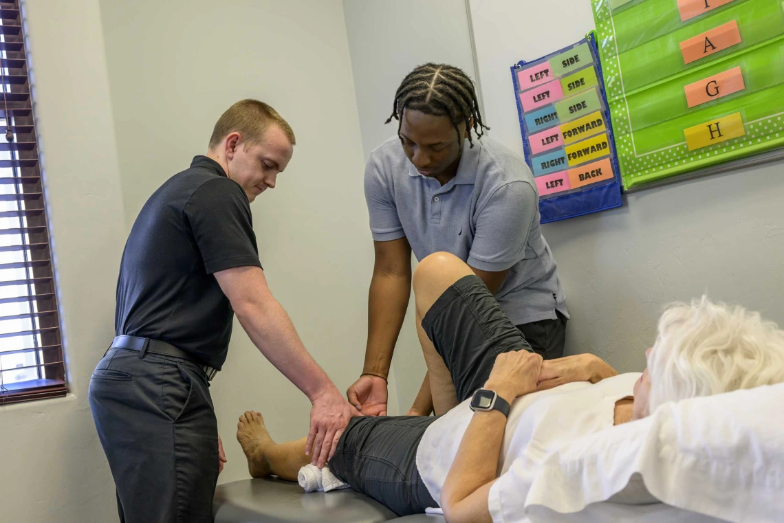 A physical therapist provides instruction to a student observing how to work with clients in a clinic.