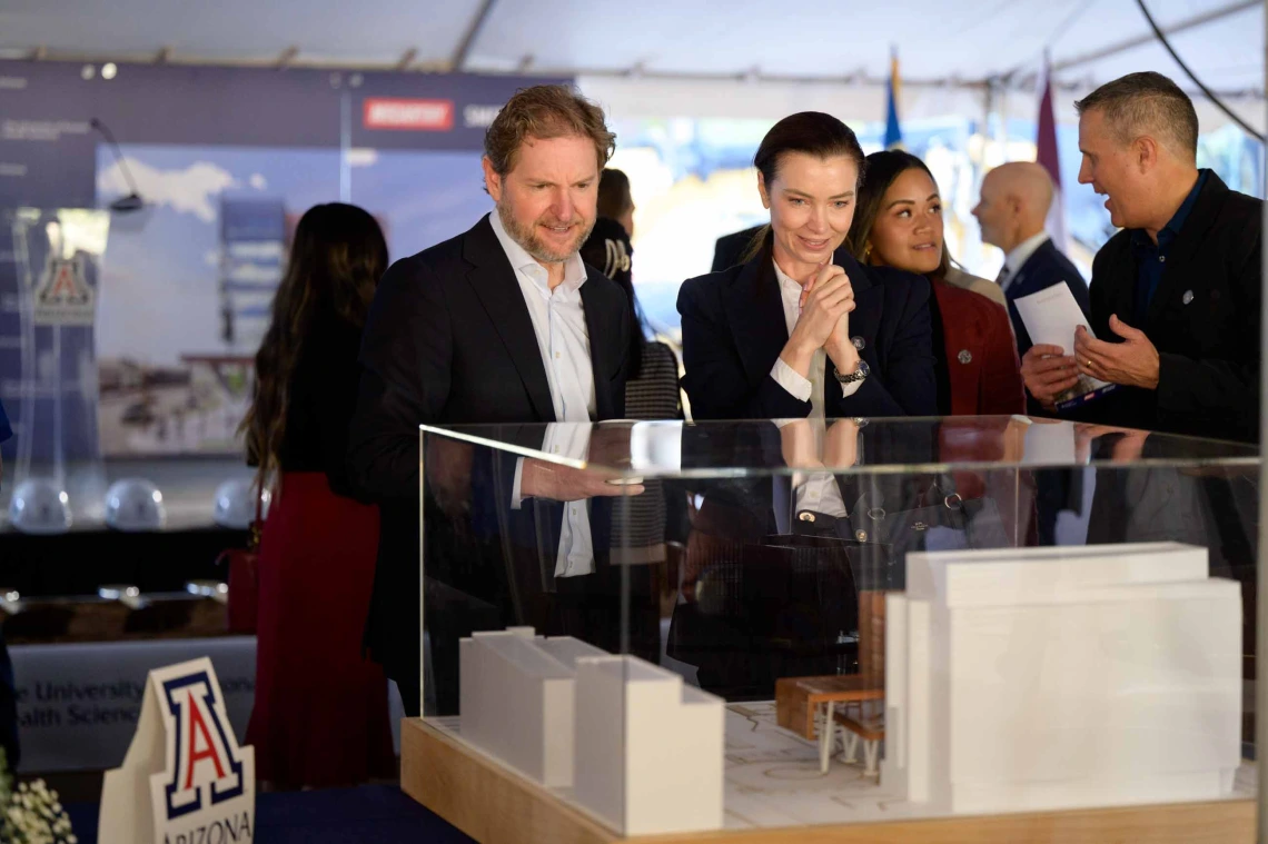 A man and woman smile as they look at a 3-D building model in a glass case. 