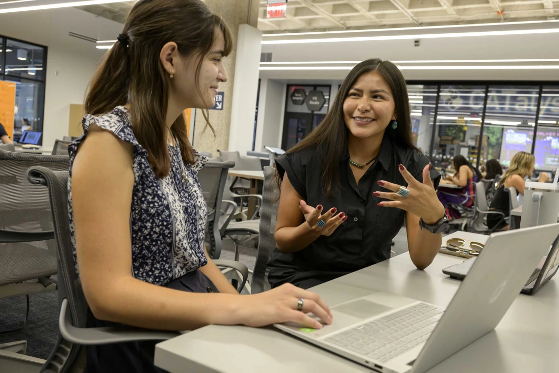 Photo of a young woman with her hand on a lap top who is looking at Caleigh Curley as Curley gestures with her hands. 