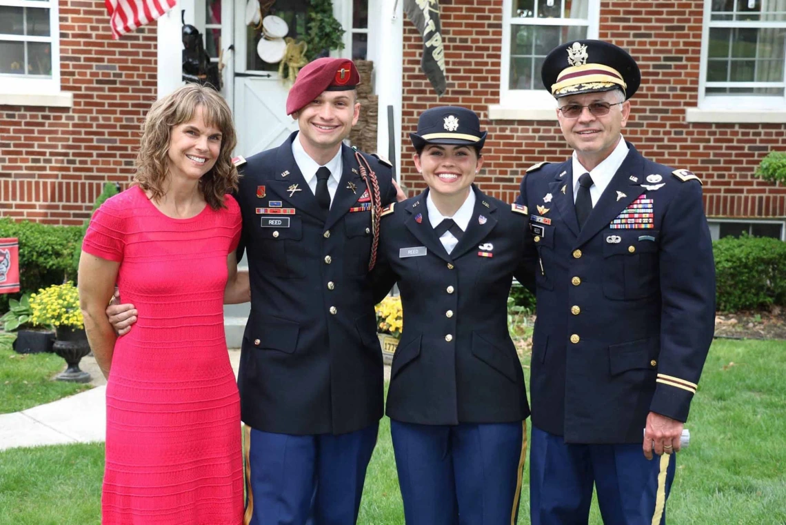 A family stands together with the father, son and daughter all in dress military uniforms while the mom is in a red dress. 