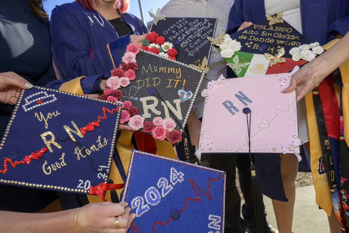 Several decorated graduation caps are held out by University of Arizona College of Nursing students. The caps have graphics and text on them noting “2024” and “RN,” along with various other messages. 