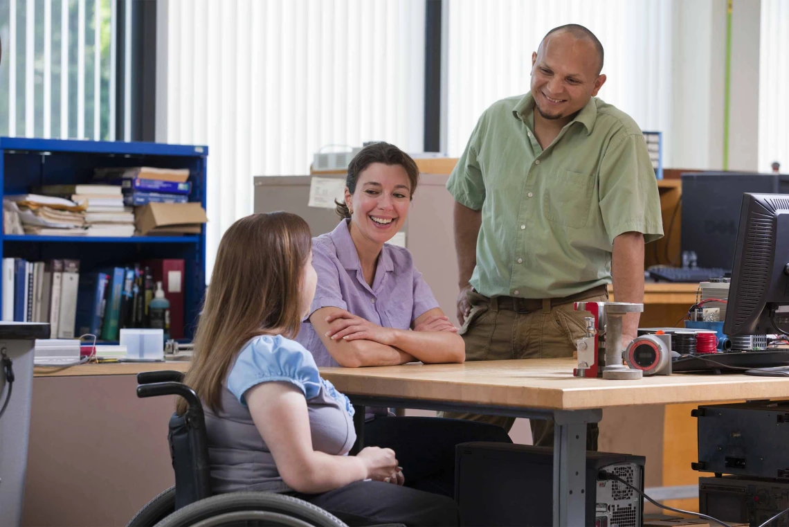 A person in a wheelchair chats with a two people in an office environment