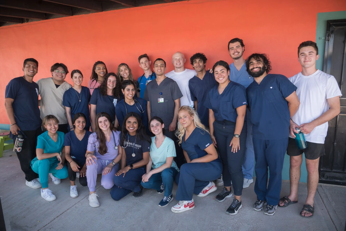 Group of young medical students wearing scrubs pose for a photo in front of a bright orange wall