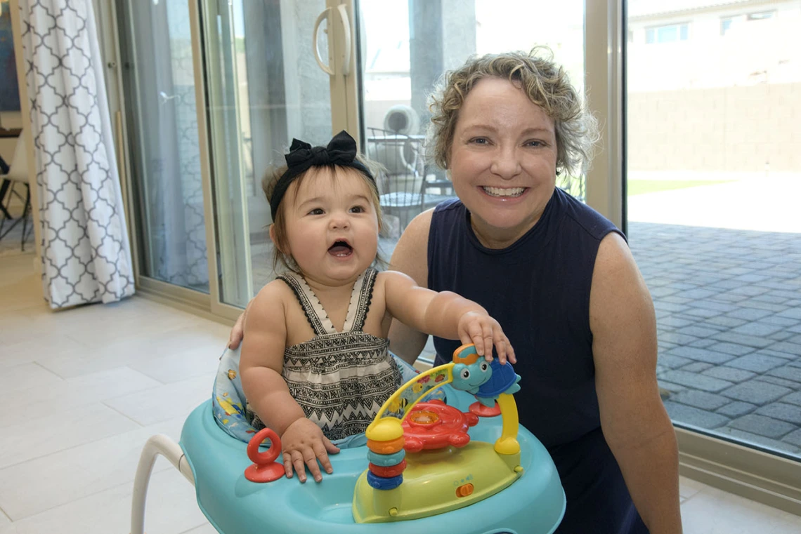 Woman crouches by a young child in a playchair.