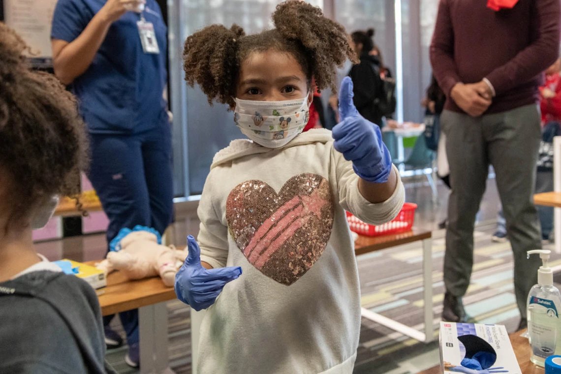 Little girl tries on gown and gloves at the Wildcat Play Hospital sponsored by the University of Arizona College of Nursing.